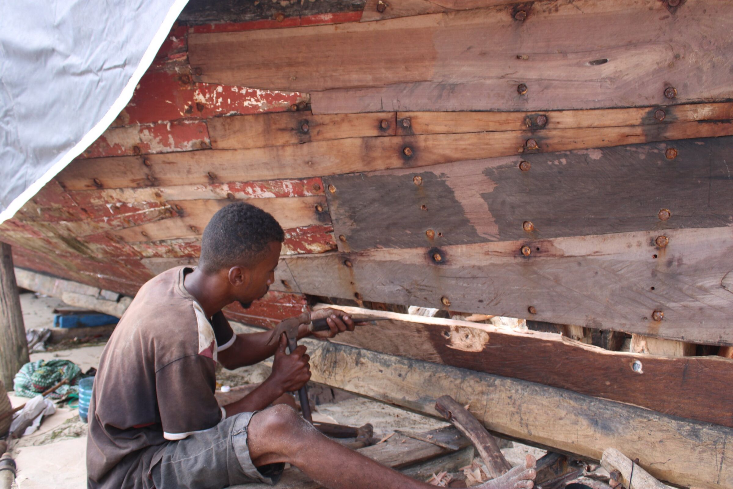 A craftsman shaping the wooden planking of a dhow hull by hand in Lamu, part of the coast's traditional boat-building industry